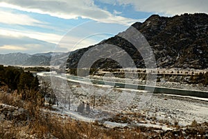 Snow-covered banks of a beautiful river flowing through a picturesque valley at the foot of high mountains in early winter