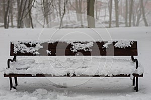 A snow-covered bench in the park. A bench covered with snow by t