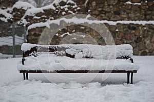A snow-covered bench in the park. A bench covered with snow by t