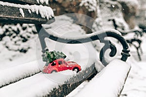 Snow-covered bench with a red toy car carrying a Christmas tree on a roof