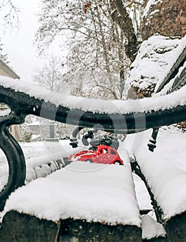 Snow-covered bench with a red toy car carrying a Christmas tree on a roof