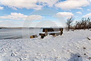 A snow covered bench with a view to the beach and River Deben at the popular visitor Bawdsey Quay on the Suffolk coast