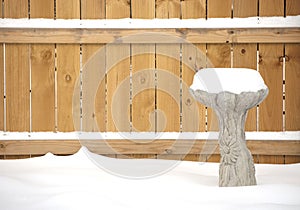 Snow covered birdbath in front of fence