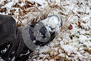 Snow-covered black boot of a man on his feet while walking in a winter park, top view. Man in black boots in the snow