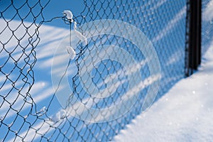 A Snow-covered Broken Steel Mesh Fence is Positioned Diagonally in the Frame. Sunny Frosty Day in the Town. Selective Focus. Close