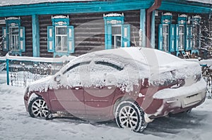 A snow-covered car parked near a house in the village. A frozen car under the snow. Selective focus