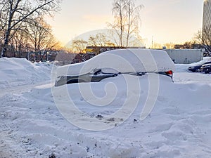 A snow-covered car in a parking lot against the background of the dawn sky.