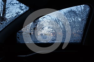 Snow-covered car side window with melted snow drops. Blurred background. Copy space