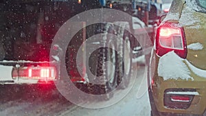 snow covered car tail light at winter day near truck during snowfall