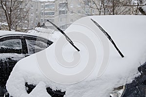 Snow-covered car with windscreen wiper during winter snowfall