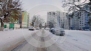 Snow-covered cars are parked along the road in a residential courtyard with an apartment buildings in winter. The danger