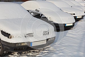 Snow covered cars parked in a row next to each other.