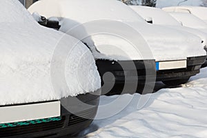 Snow covered cars parked in a row next to each other.