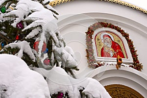 Snow-covered Christmas tree branch on the background of the Orthodox icon and the cross. Orthodox Church Winter - Christmas.