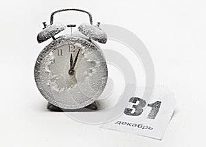 Snow-covered clock-alarm clock and crumpled sheet of tear-off calendar, written in Russian .