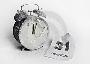 Snow-covered clock-alarm clock and crumpled sheet of tear-off calendar, written in Russian .