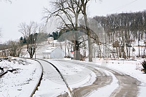 Snow covered country road and railroad tracks, in a rural area o
