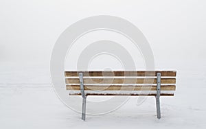 Snow covered empty wooden bench in a ghostly winter fog