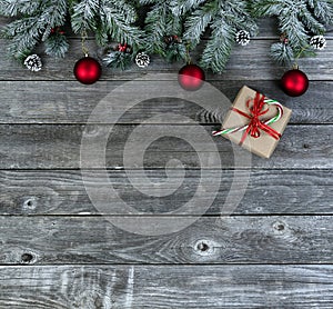 Snow covered evergreen branches plus bright red ornaments and gift box on faded wooden planks for a merry Christmas or happy New