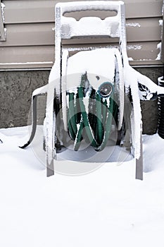 Snow covered garden hose ouside a house in winter