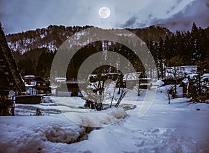 Snow covered ground in winter. Town with night sky and full moon