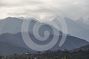 Snow-covered high mountains of the Zailiyskiy Alatau over houses on a hillside in gray overcast rainy cloudy weather