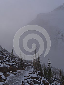 Snow-covered hiking trail on slope in front of the rugged rock face of Mount Edith Cavell in Jasper National Park, Canada.