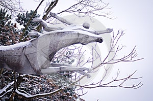 Snow covered horse statue flying with his rider, trees background