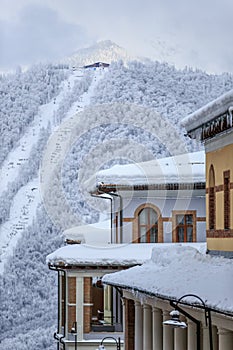 Snow covered hotel roofs of Gorky Gorod winter mountain resort with cableway lift on the background vertical scenery