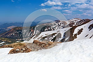 From the snow covered lawn opens a view of high mountains with snow covered tops, blue sky. Magnificent spring landscape.