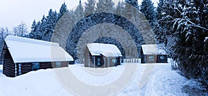 Snow covered log cabins in the woods in a forest.