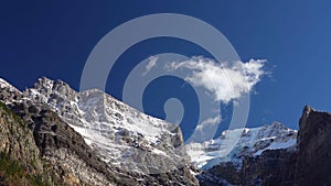 Snow-covered majestic mountain peaks with dark blue sky and flowing clouds