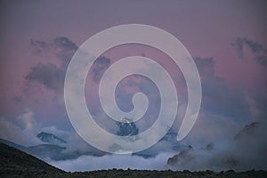 Snow covered mountain peak rises above the clouds under a twilight sky