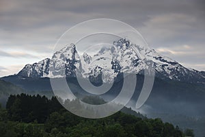 Snow covered mountain peak of Watzmann at Berchtesgaden with clouds and morning fog during sunrise, Bavaria