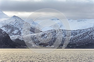 Snow-Covered Mountain Range Overlooking the Calm Sea Under Cloudy Skies