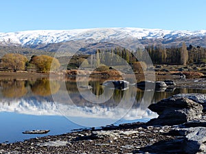 Snow covered mountain range reflected in lake at Butcher's Dam, Central Otago, New Zealand