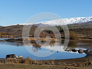 Snow covered mountain range reflected in lake at Butcher's Dam, Central Otago, New Zealand