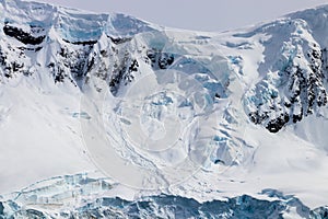 Snow covered mountain ridge, Antarctica. Rocks, blue ice. Cloudy sky.