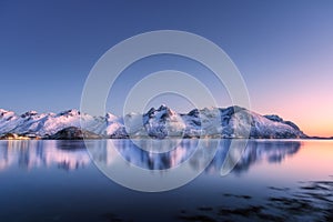 Snow covered mountains and colorful sky reflected in water