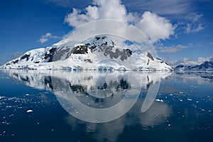 Snow covered mountains and glaciers in Antarctca reflecting in dark blue sea with ice floes, Paradise Bay