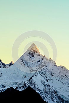 snow covered mountains with one large peak in the distance during sunset