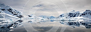 Snow covered mountains reflected on still water with cloudy sky, Paradise Habour, Antarctica