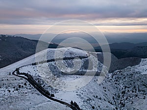 snow covered mountains at sunset with a winding road in the foreground aerial view