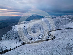 snow covered mountains at sunset with a winding road in the foreground aerial view