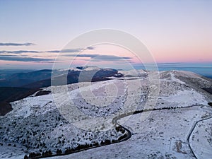 snow covered mountains at sunset with a winding road in the foreground aerial view