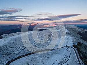 snow covered mountains at sunset with a winding road in the foreground aerial view