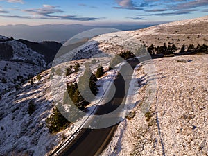 snow covered mountains at sunset with a winding road in the foreground aerial view