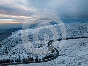 snow covered mountains at sunset with a winding road in the foreground aerial view