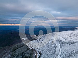 snow covered mountains at sunset with a winding road in the foreground aerial view