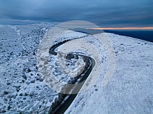 snow covered mountains at sunset with a winding road in the foreground aerial view